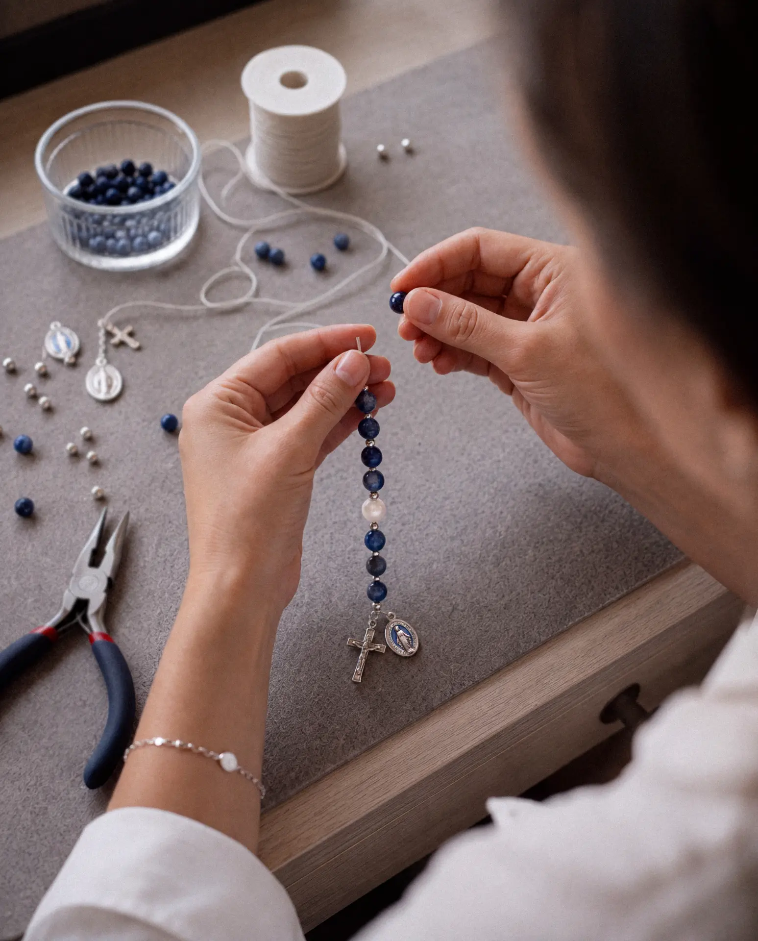 Hands knotting a rosary at a workbench